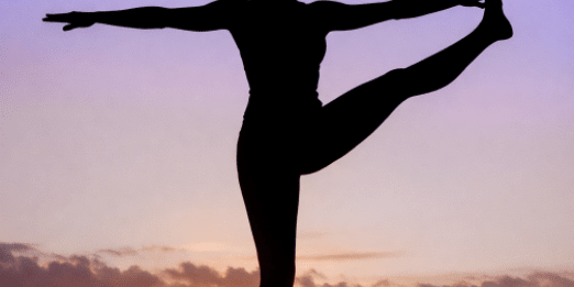 Silhouette of a person balancing in a yoga pose on one leg at sunrise, with the sun low on the horizon and a gradient sky shifting from orange to purple.